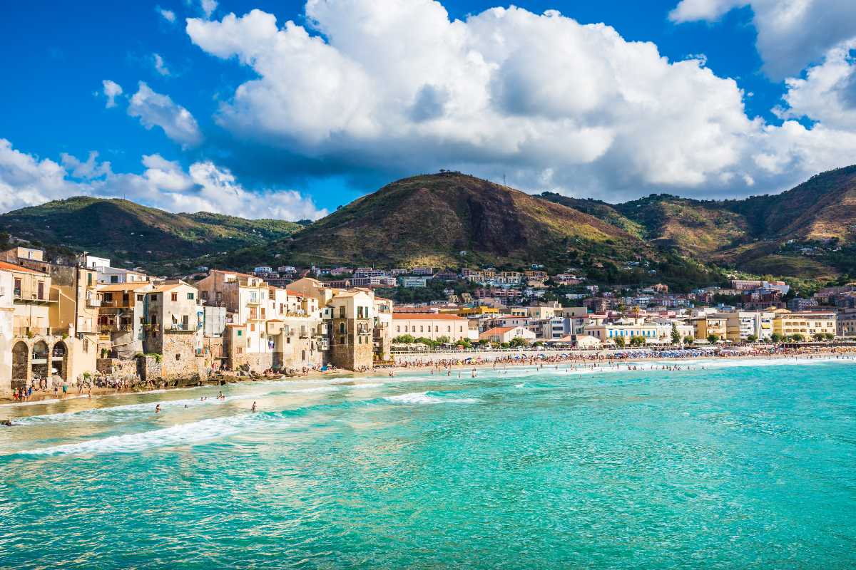 Vista panoramica di Cefalù al tramonto dal lungomare, con la Rocca e la Cattedrale illuminate dalla luce dorata e il mare calmo