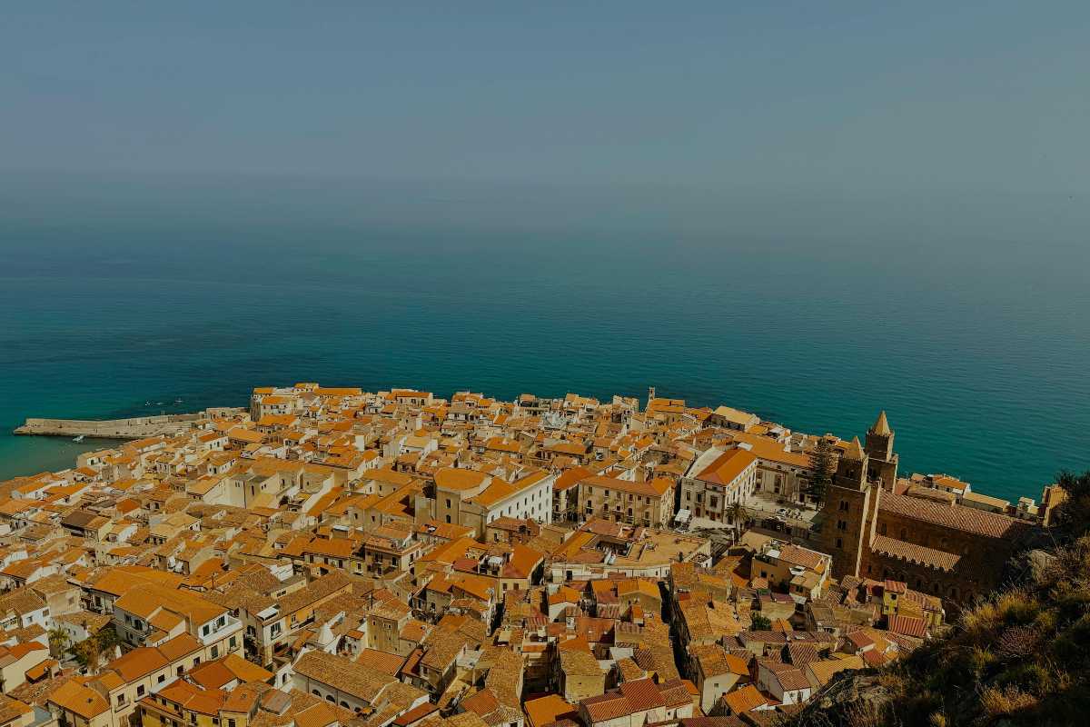 Gruppo di escursionisti lungo un sentiero tra pini e rocce sulle Madonie, con vista sul mare e Cefalù in lontananza, giornata primaverile