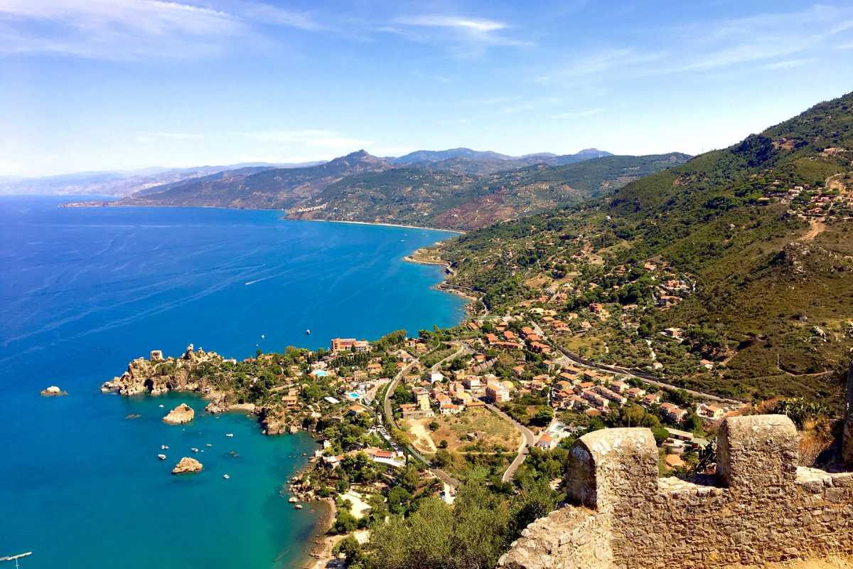 Scorcio di una famiglia che cammina lungo il sentiero della Rocca di Cefalù con vista sul mare e sul paese, luce naturale e atmosfera di avventura
