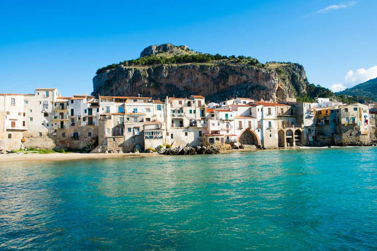 Scatto serale durante la festa del SS. Salvatore a Cefalù, folla sul molo, barche illuminate, fuochi d’artificio sul mare